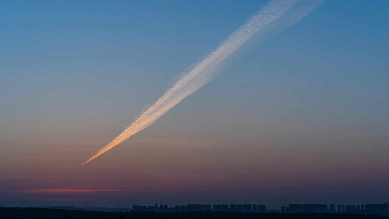Dramatic Airplane Contrail at Sunset over a City Horizon