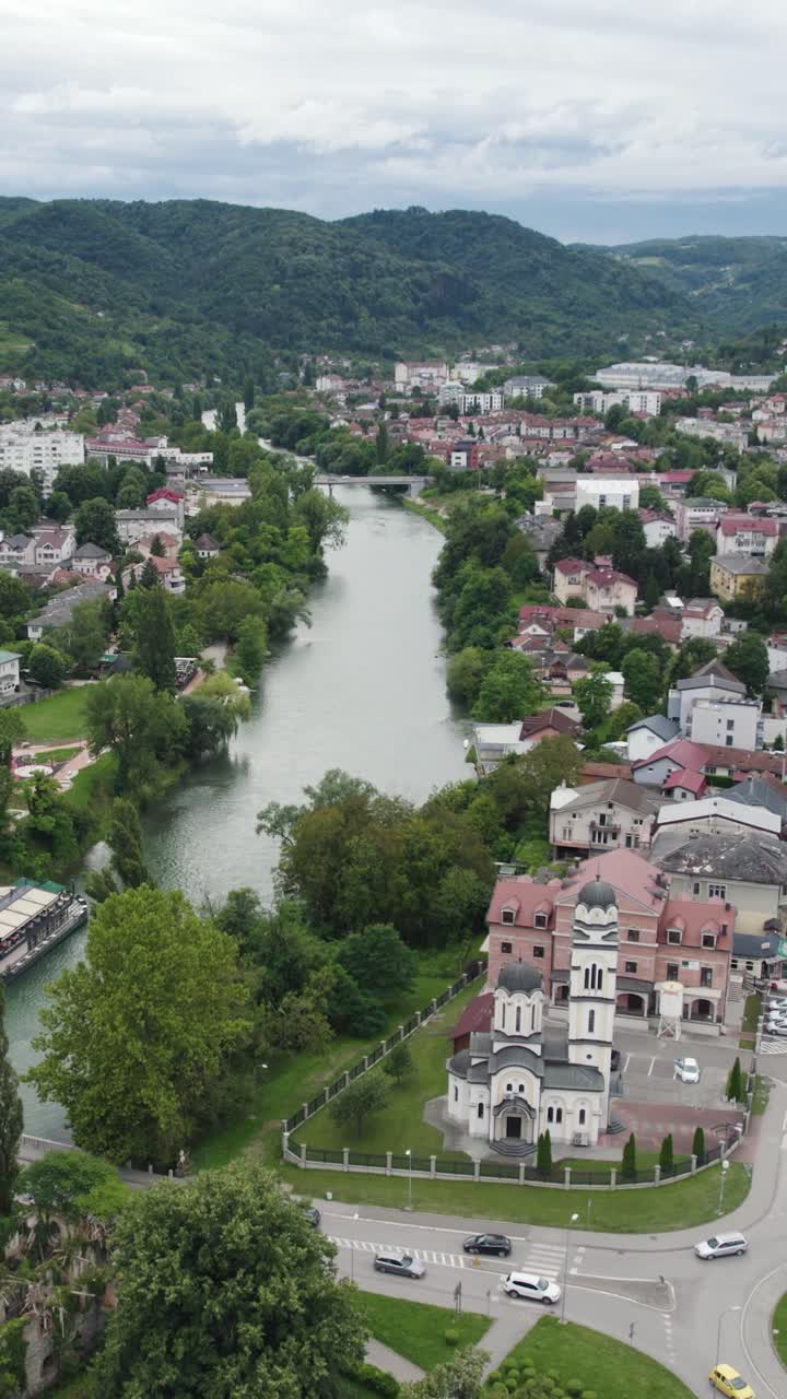 Vrbas River meandering through the cityscape of Banja Luka in Bosnia and Herzegovina, featuring a church and lush greenery. Aerial Dolly, Vertical Video