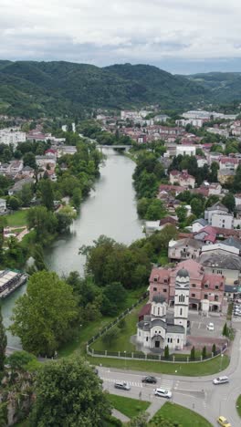 vrbas river meandering through the cityscape of banja luka in bosnia and herzegovina, featuring a church and lush greenery. aerial dolly, vertical video