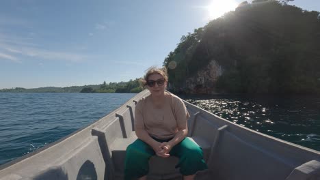 happy woman sits on bow of a boat sailing through famous kali biru in indonesia