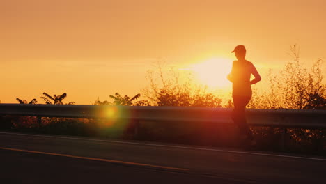 silhouette of a young active woman jogging along a highway near the sea at sunset