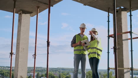 Professional-engineers-in-safety-vests-and-helmets-working-with-digital-tablet-and-blueprints