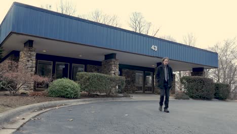 man walking out of a generic commercial building wearing a black coat and tie