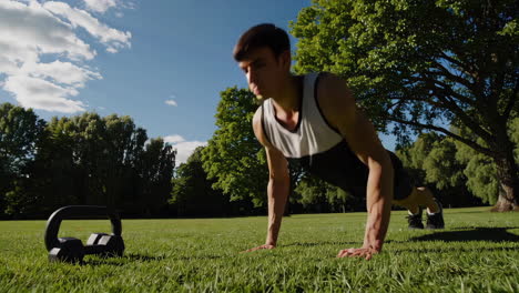 man performing push-ups in a park with a kettlebell