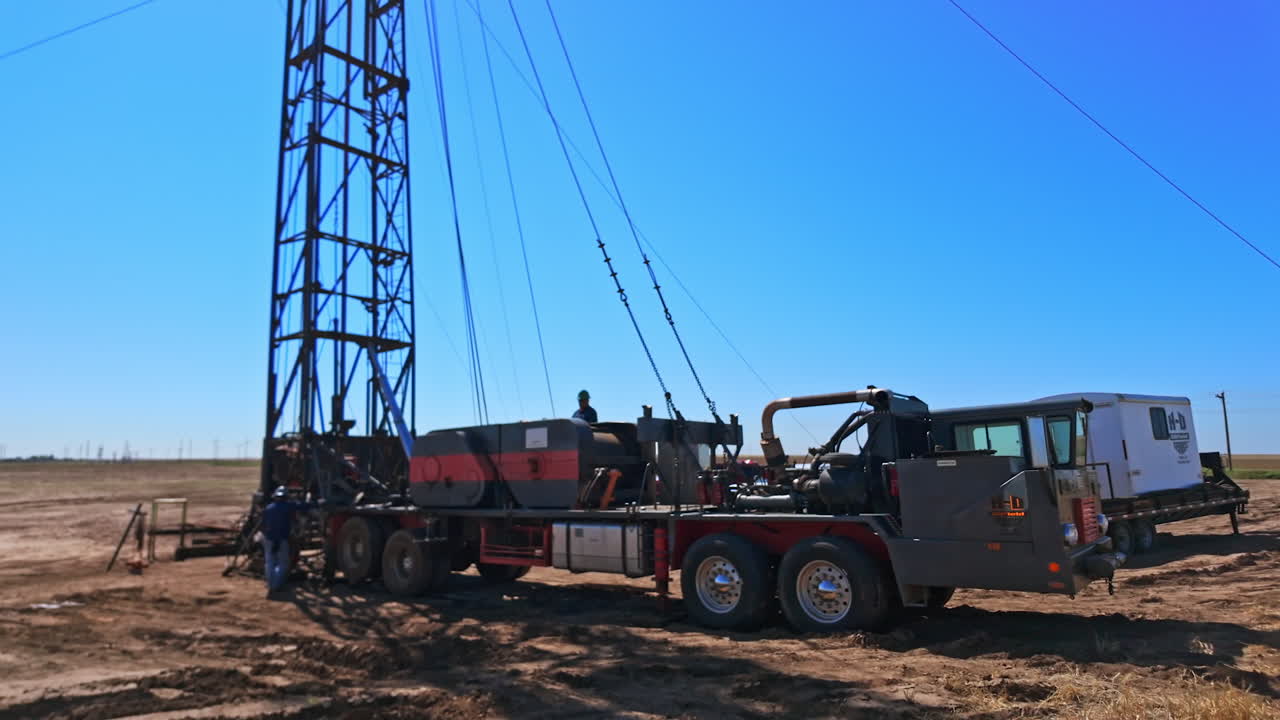 Approaching the machine with the derrick for drilling ground. Men work at the equipment for boring oil in the desert.