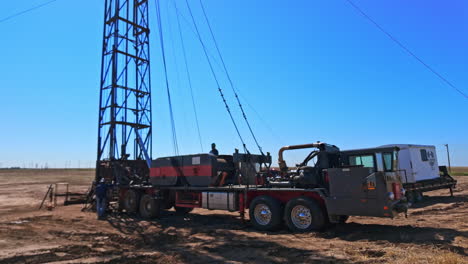 approaching the machine with the derrick for drilling ground. men work at the equipment for boring oil in the desert.