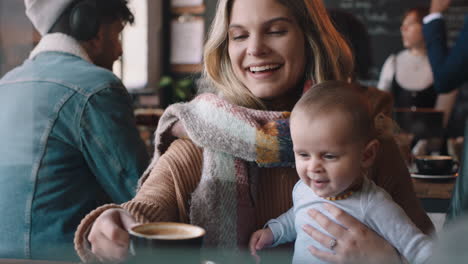 young mother with baby in cafe using smartphone drinking coffee relaxing in busy restaurant enjoying motherhood