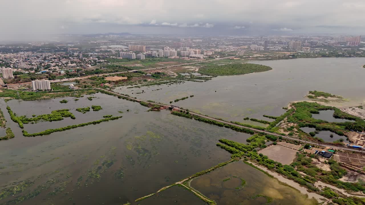 Aerial shot of flooded landscape with road cutting across it with a cityscape at background. Cloudy day.