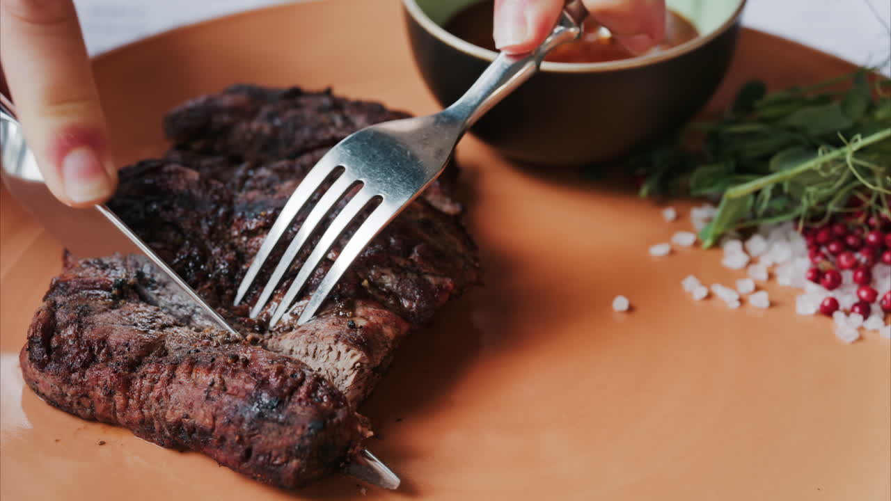 Close up of a woman's hands cutting a Sirloin Steak with Barbecue Sauce and micro-plants on the side