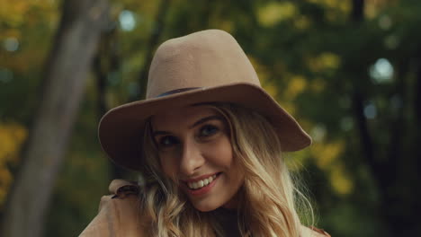 vista de cerca de una joven rubia caucásica con un sombrero sonriendo y mirando la cámara en el parque en otoño