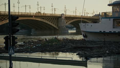 bridge and boat beside a large pile of flood debris in the river, with traffic signals in the foreground, budapest, hungary