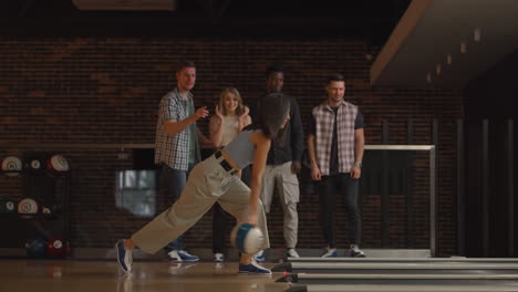 a young brunette woman makes the final throw with a bowling ball and wins the game with the support and joy of her friends of different nationalities. rejoice and celebrate the victory