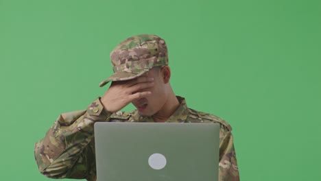 close up of asian man soldier using a laptop and having a headache while standing in the green screen background studio