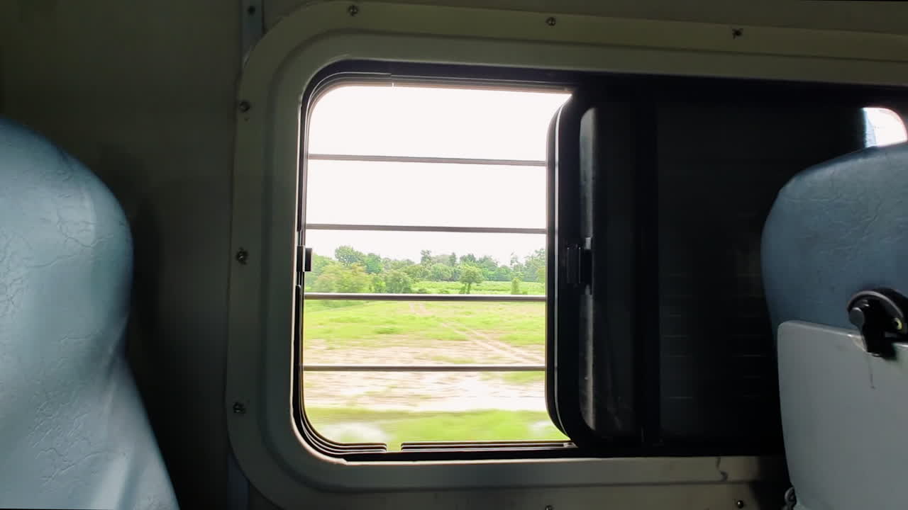 View from small train window as it rides through scenic Indian countryside, lush green fields, clusters of trees.