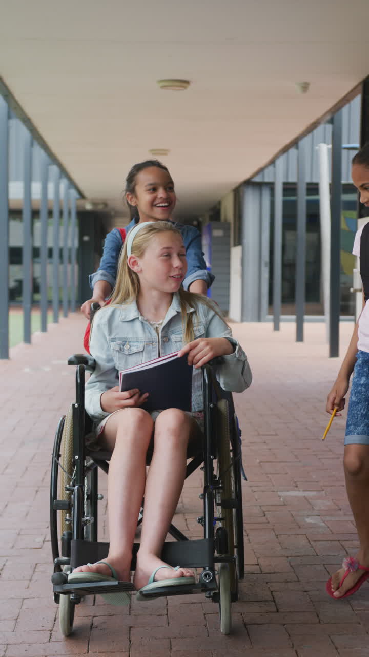 Vertical video three diverse, happy girls talking in school corridor, one in wheelchair, copy space