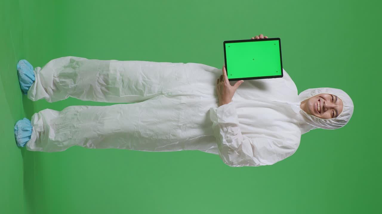 cuerpo lleno de científico masculino asiático sonriendo y mostrando la tableta de pantalla verde mientras está de pie en el fondo de la pantalla verde
