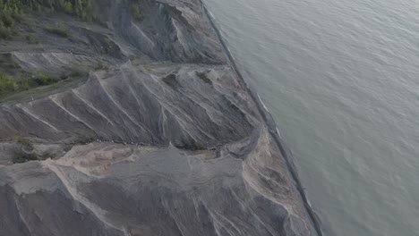 Drone-shot,-flying-down-with-the-camera-panning-up-and-to-the-right,-showing-the-coast-line-of-a-lake-and-carved-out-rock-formations