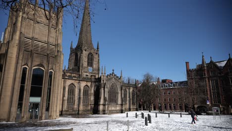 Man-walks-in-front-of-snowy-cathedral-on-sunny-day,-Sheffield,-wide-angle