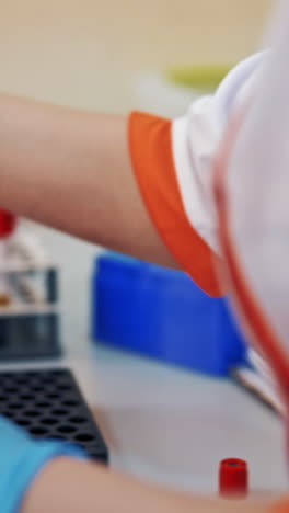 laboratory worker is putting tubes with blood on a rack. hands of a female nurse in sterile gloves working with vials on the table in a laboratory. close-up. vertical video