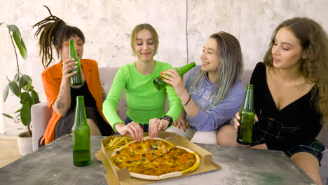 four friends eating pizza and drinking beer while having a good time on a home party