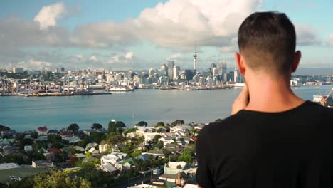 slowmo - caucasian male from behind taking photo of auckland downtown, new zealand