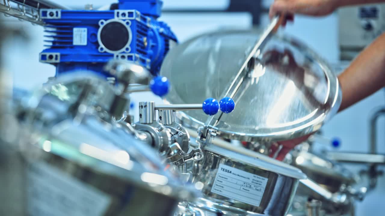Modern factory of dairy products indoors. Worker opens metal mixer inside the milk plant. Cheese production process. Contemporary equipment for making fresh cheese. Close-up.