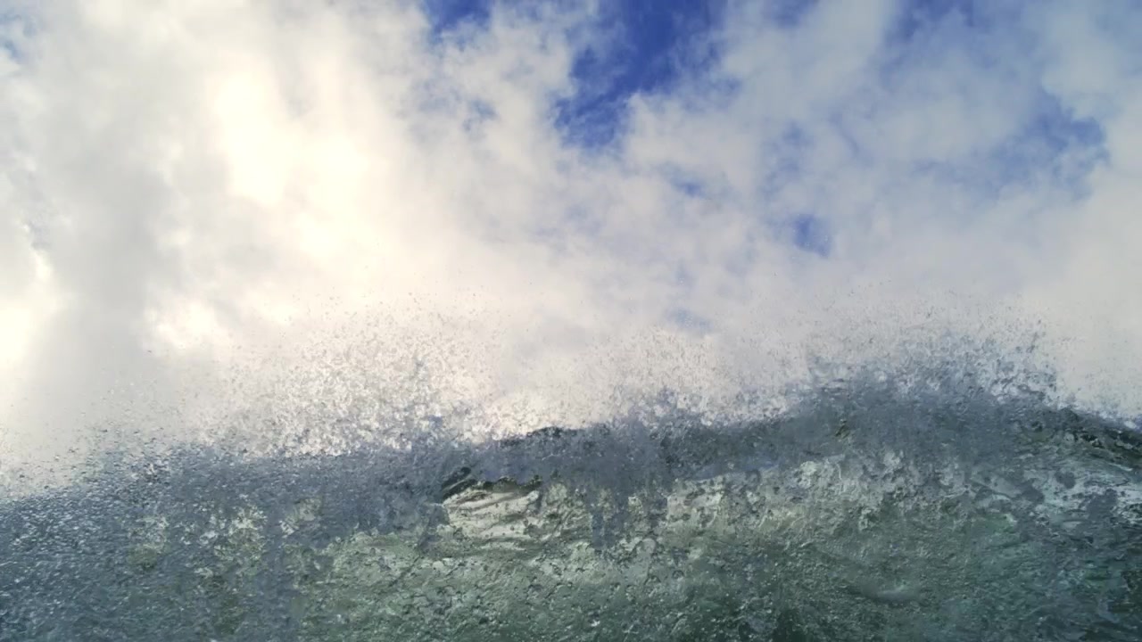 Windblown ocean swell throws fine spray beneath dense white clouds in prolonged slow motion