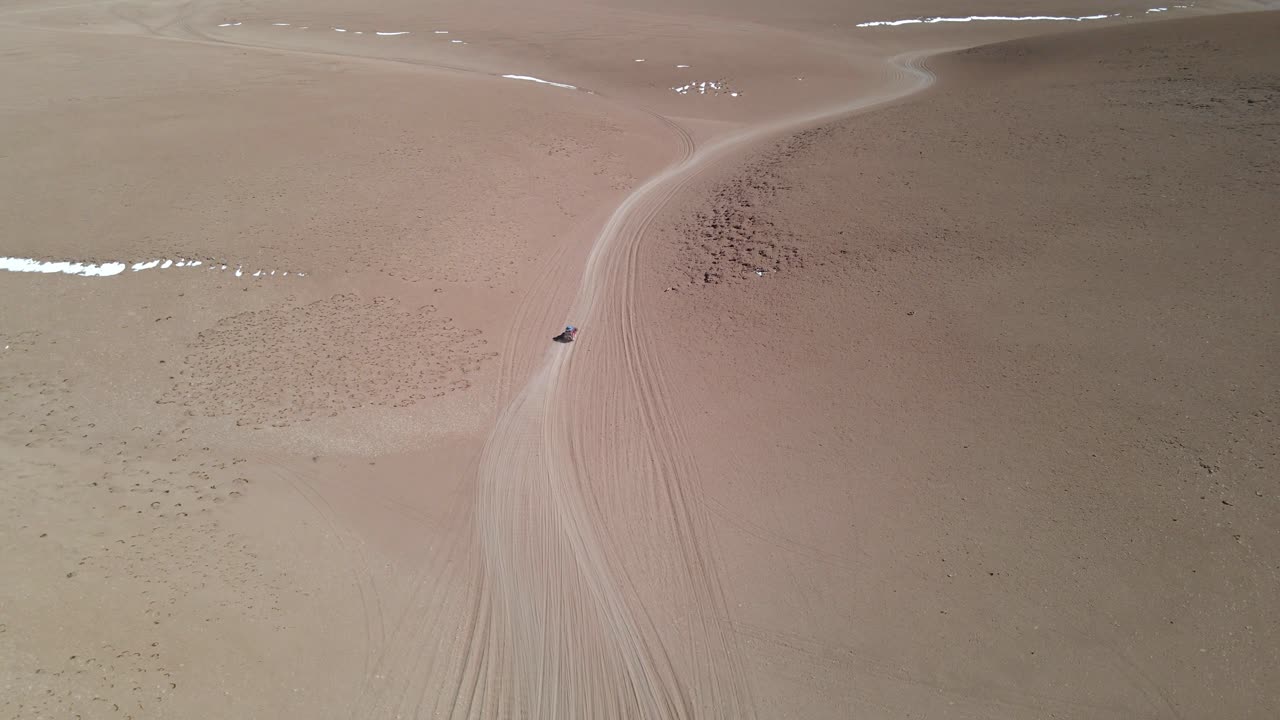 Curved dirt road stretches across dry desert plain in Bolivia, shown from high drone angle