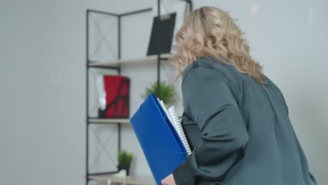 ceo walks into bright office holding coffee and business files, preparing for workday as she approaches desk to place items down and access laptop in professionally equipped workspace