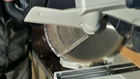 un joven con barba en un mono gris de profesión un carpintero trabaja con una máquina de corte circular en su taller de casa