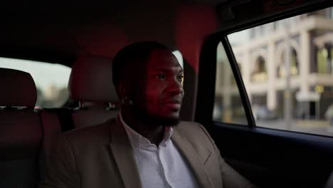 a happy man with black skin and a beard a businessman in a brown suit rides in a modern car interior around the city during his business trip