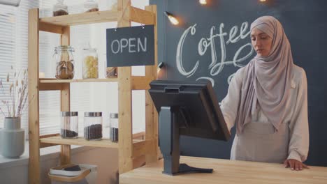 una camarera en una cafetería cuelga el letrero cerrado y se quita el delantal detrás del mostrador