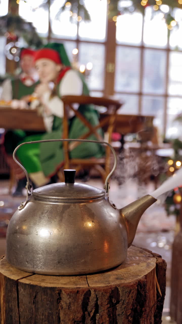 Boiling retro aluminium kettle. Teapot steams. Two elves on the background. New year spirit. Christmas eve. Closeup. Teapot on a log. Vertical video