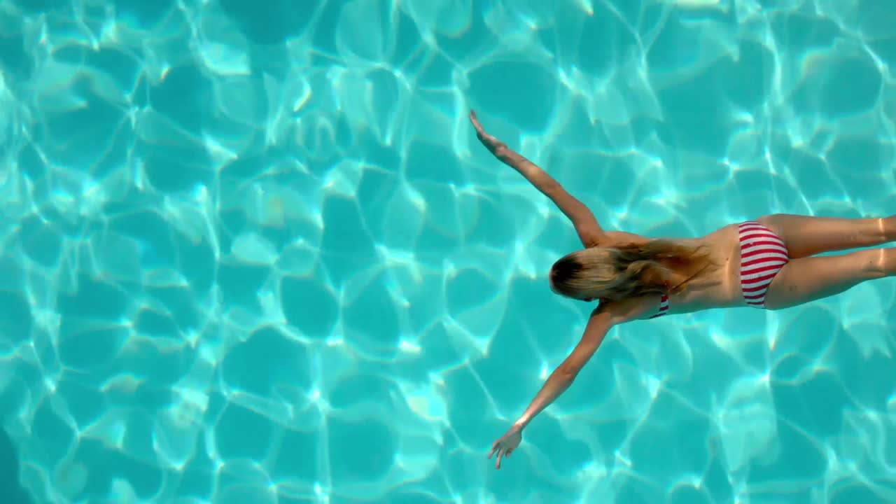 Wanita menyelam di kolam renang dengan pemandangan dari atas.