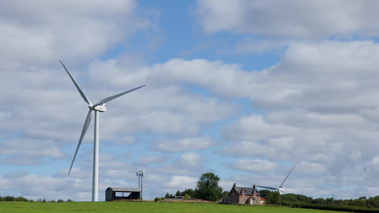 Large wind turbine spins steadily in open green field, daylight, wide shot, partly cloudy sky