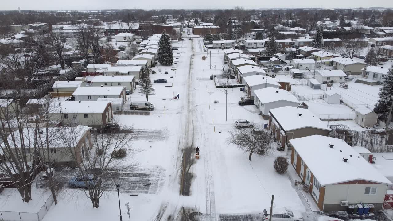 Snow-covered suburban street in St-Constant, Québec, with houses and a lone pedestrian