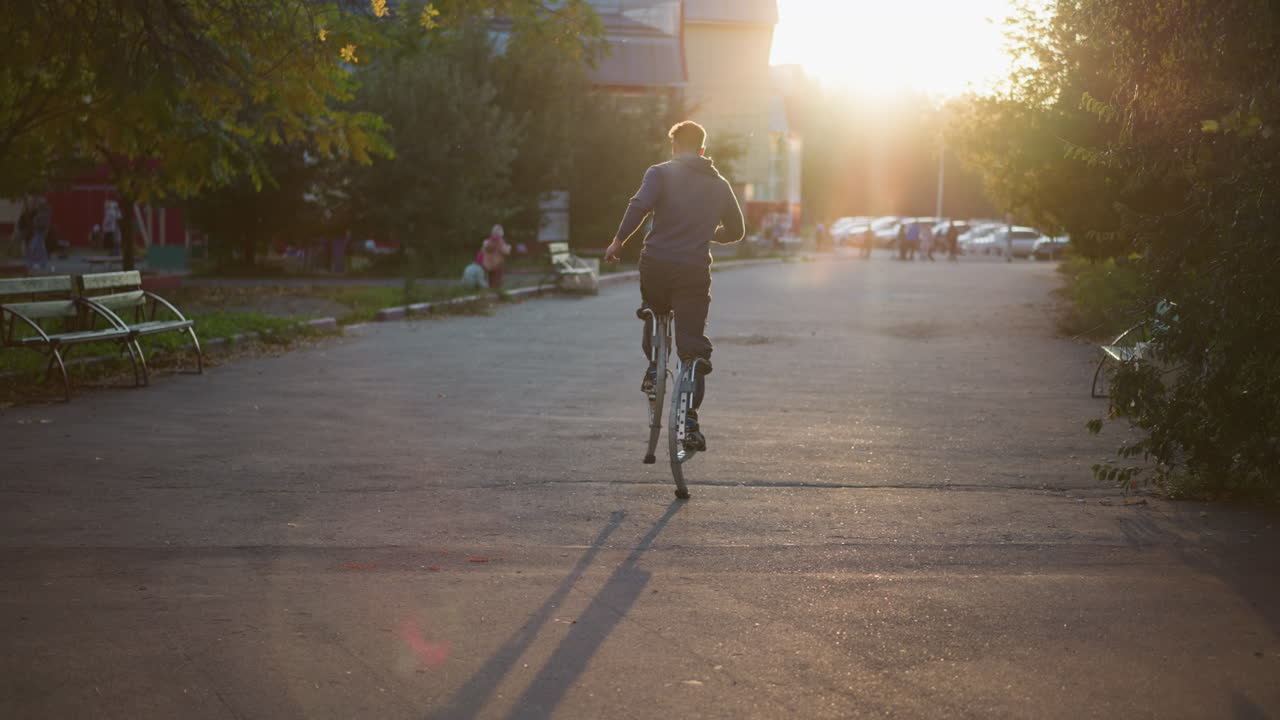 주거 지역의 포장 된 도로를 따라 발바닥에 달리는 젊은 남성, 늦은 오후 또는 이른 저녁에 뒤에서 잡혔습니다. 어두운 회색 파란색 스웨트 셔츠와 어두운 바지를 입고, 부드러운 빛으로