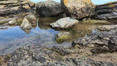 low right-sliding camera glides across beach front rocks, capturing trapped seawater that mirrors moody sky above. ideal for meditative or nature documentaries