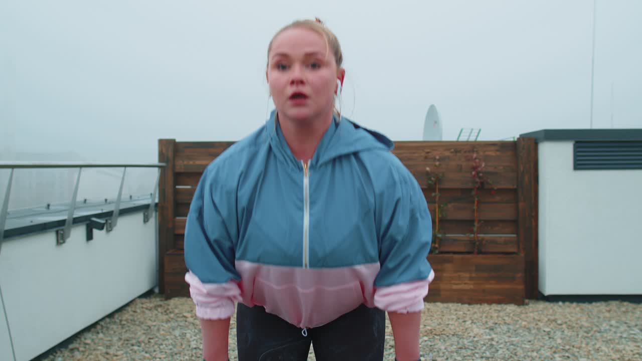 스포츠 의류 를 입은 스포츠 소녀 는 야외 에 있는 집 지붕 에 고무 밴드 를 사용 하여 요가 스트레칭 운동 을 한다