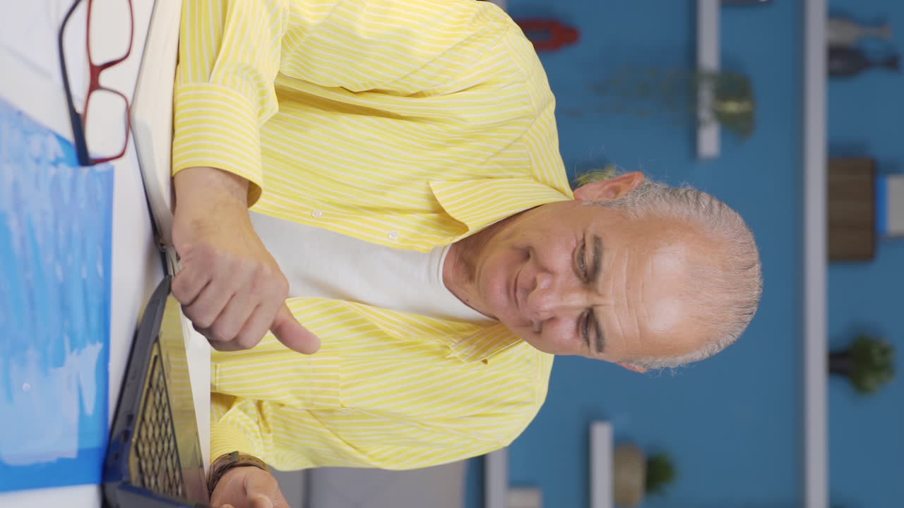 홈 오피스 직원의 수직 비디오 노인이 노트북을 사용하여 재미있게 일합니다.