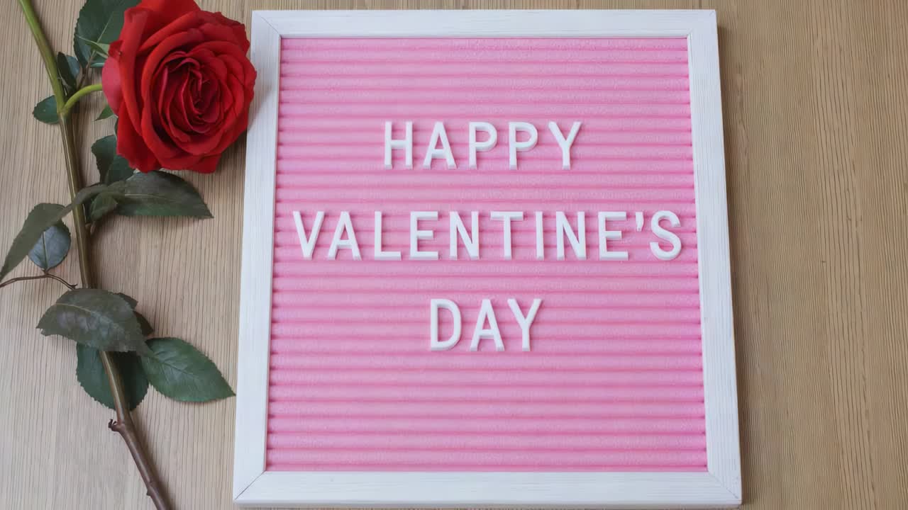 Light activating, pink letterboard glowing HAPPY VALENTINE'S DAY on wood table and red rose left