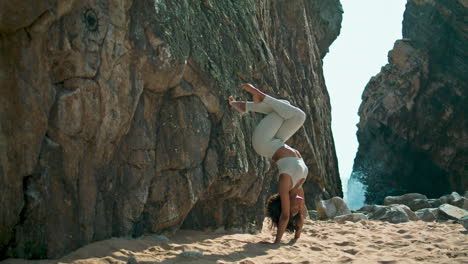 niña yogi de pie al revés en la playa rocosa de ursa. mujer haciendo asana de yoga