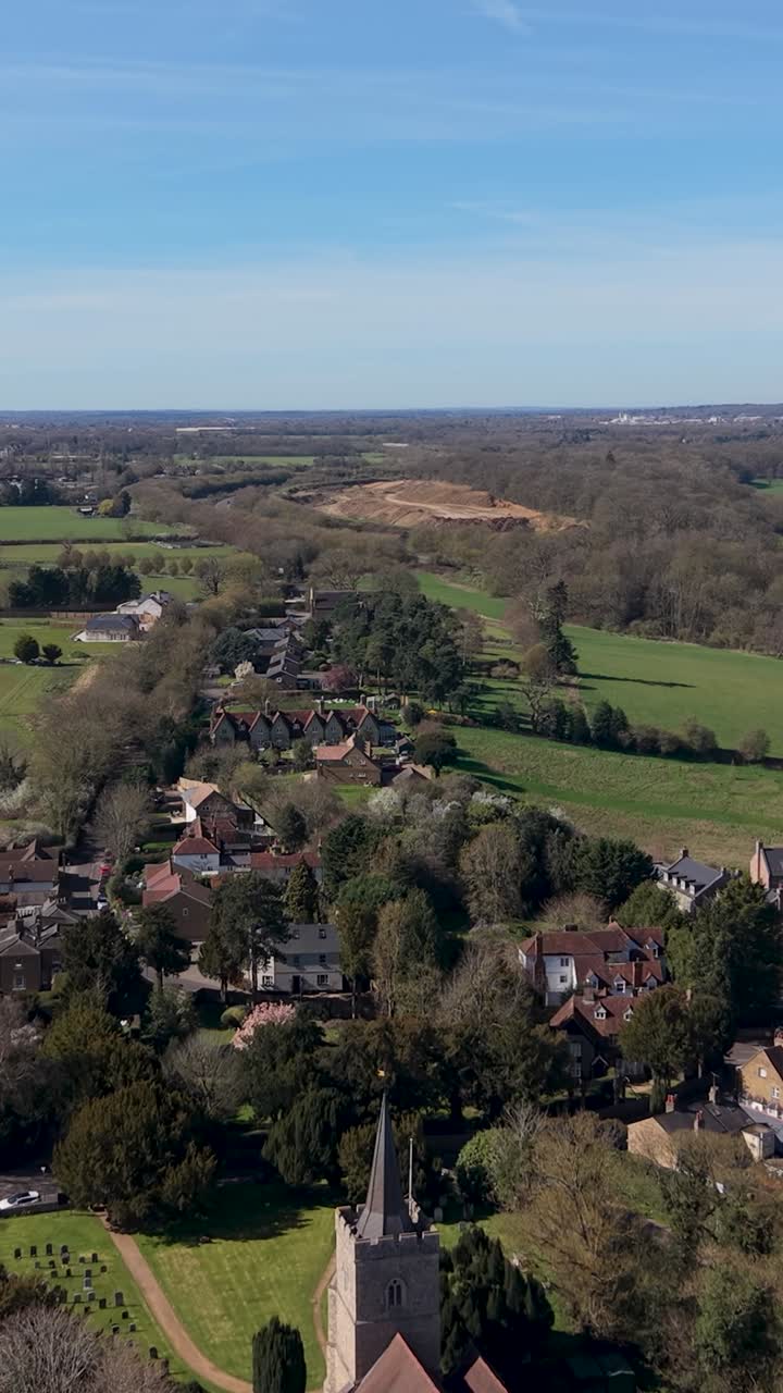 Hertingfordbury vertical drone flight over St Mary's church and village, gliding toward Panshanger quarry on a bright spring day with green fields, countryside homes, and clear skies