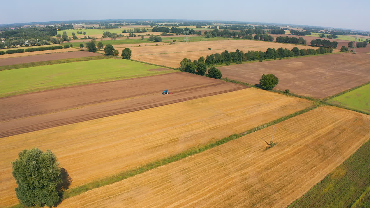Aerial view of drone flying above farmland with tractor on the field