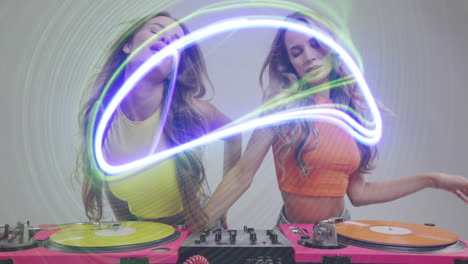 identical twin female djs dancing behind record turntables and ovelrayed disco lights