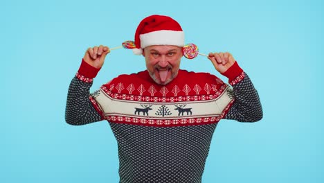 Funny-man-in-red-New-Year-sweater-holding-candy-striped-lollipops-hiding-behind-them,-fooling-around