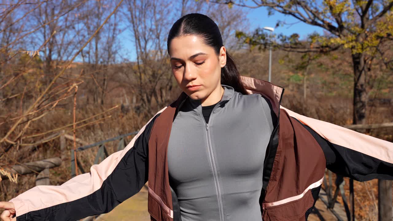 Sexy fit brunette jogger fastening her jacket at the park