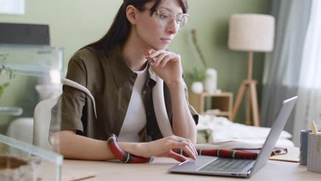 Mujer-Joven-Que-Trabaja-En-Una-Computadora-Portátil-Mientras-Sus-Dos-Serpientes-Mascota-Se-Deslizan-Sobre-La-Mesa-Y-Alrededor-De-Ella