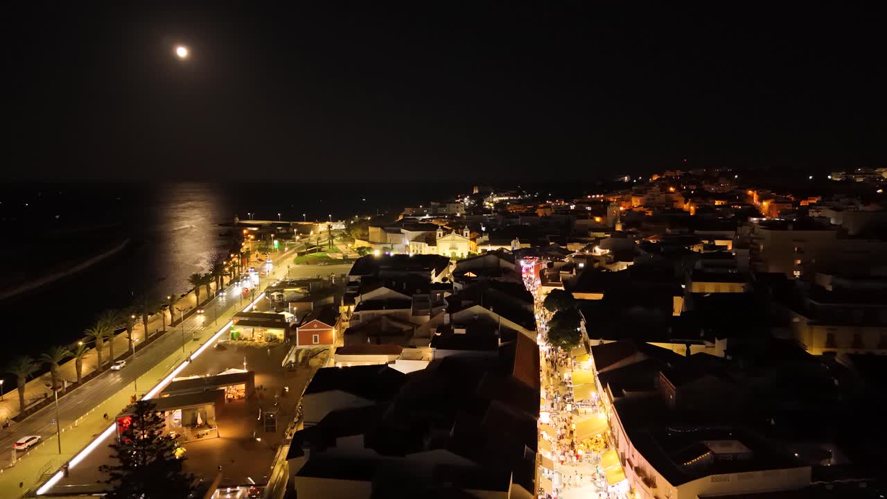 Aerial view of Lagos illuminated cityscape by night with the full moon reflecting on the ocean, Portugal