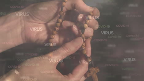 covid-19 and virus text against hands praying and holding rosary